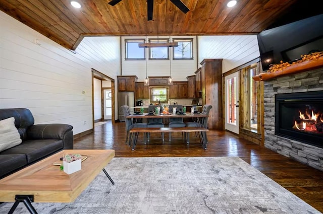 living room featuring ceiling fan, dark wood-type flooring, a stone fireplace, wooden walls, and wood ceiling