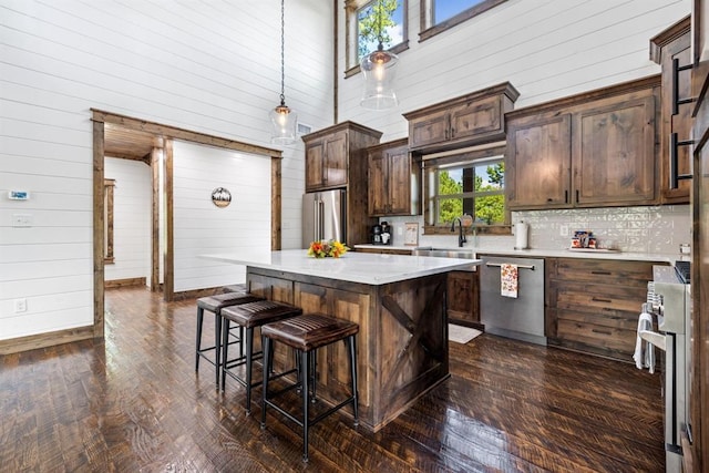 kitchen with a towering ceiling, dark brown cabinetry, stainless steel appliances, a kitchen island, and hanging light fixtures