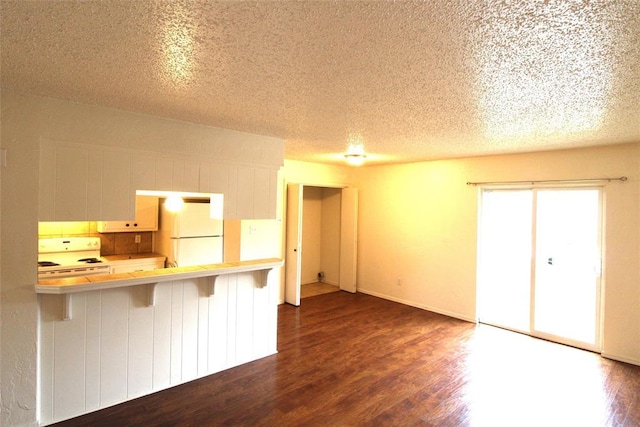 kitchen featuring a kitchen breakfast bar, dark hardwood / wood-style floors, kitchen peninsula, and white appliances