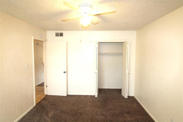 unfurnished bedroom with ceiling fan, a textured ceiling, a closet, and dark colored carpet