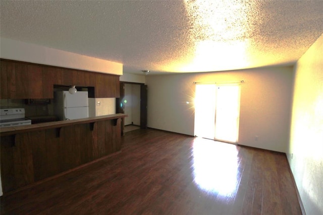 kitchen with a textured ceiling, dark wood-type flooring, a kitchen bar, and white appliances