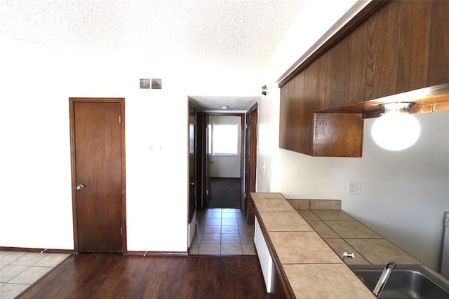 kitchen with tile counters, sink, a textured ceiling, and light hardwood / wood-style floors