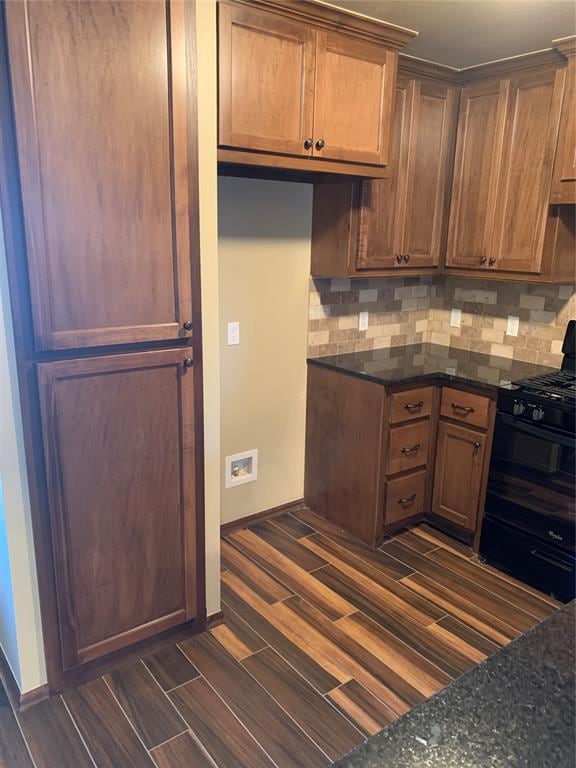 kitchen featuring black gas range, dark hardwood / wood-style flooring, dark stone countertops, and decorative backsplash