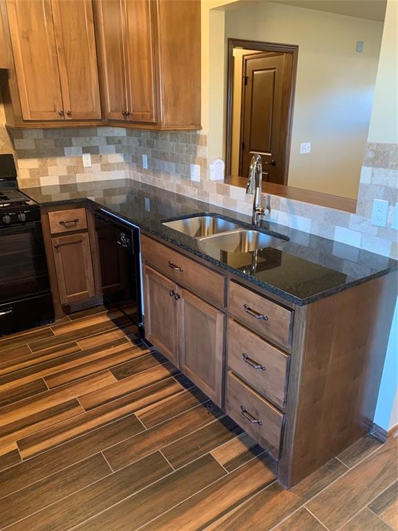 kitchen featuring sink, backsplash, kitchen peninsula, dark stone counters, and black appliances