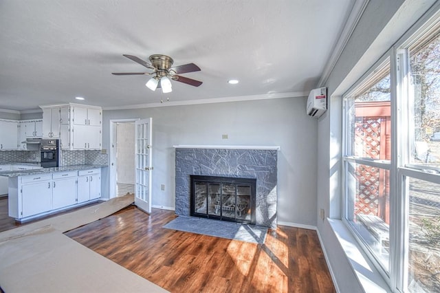 living room with a stone fireplace, an AC wall unit, ceiling fan, ornamental molding, and dark hardwood / wood-style flooring