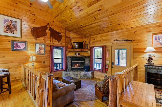 living room featuring a stone fireplace, a wealth of natural light, light hardwood / wood-style flooring, and wood walls