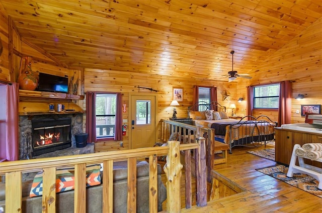 bedroom with wood ceiling, hardwood / wood-style flooring, high vaulted ceiling, a stone fireplace, and wood walls