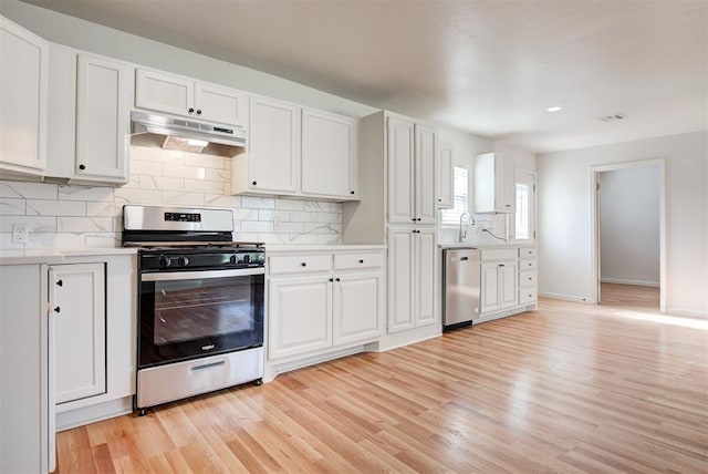 kitchen with tasteful backsplash, white cabinetry, stainless steel appliances, and light hardwood / wood-style flooring