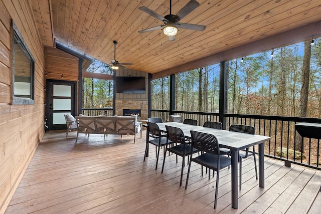 sunroom with an outdoor stone fireplace, ceiling fan, wood ceiling, and vaulted ceiling