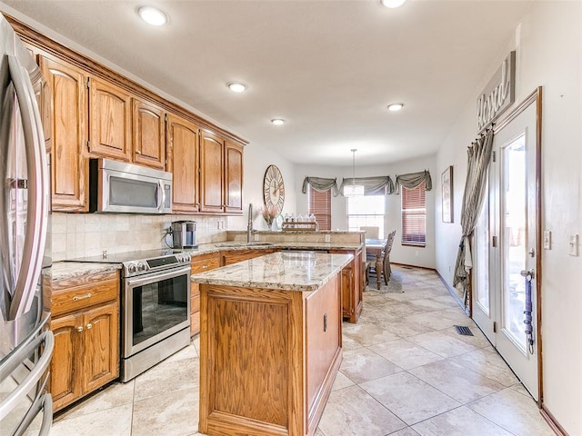 kitchen with backsplash, stainless steel appliances, sink, a kitchen island, and hanging light fixtures