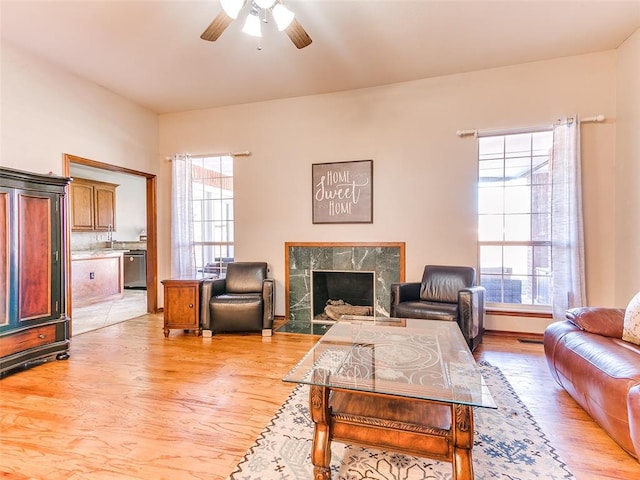 living room featuring ceiling fan, a tile fireplace, a wealth of natural light, and light hardwood / wood-style flooring