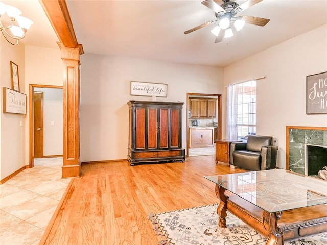 living room with decorative columns, ceiling fan, beamed ceiling, light hardwood / wood-style floors, and a tiled fireplace