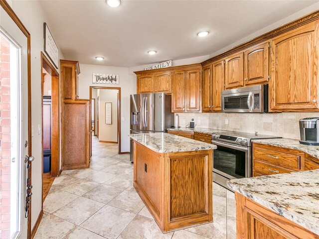 kitchen featuring a kitchen island, light stone countertops, backsplash, and appliances with stainless steel finishes