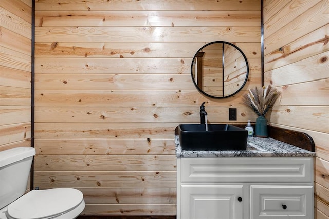 bathroom featuring vanity, wood walls, and toilet