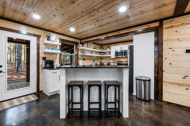 bar featuring white cabinets, wooden walls, stainless steel appliances, and dark stone counters