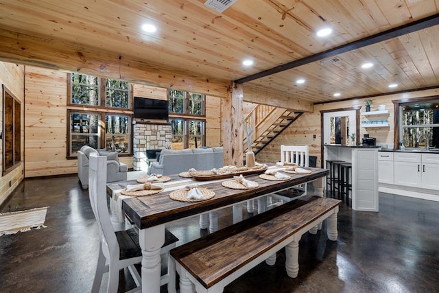 dining area featuring a stone fireplace, plenty of natural light, and wooden walls