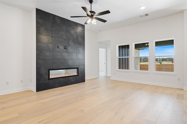 unfurnished living room featuring a fireplace, light hardwood / wood-style flooring, ceiling fan, and tile walls