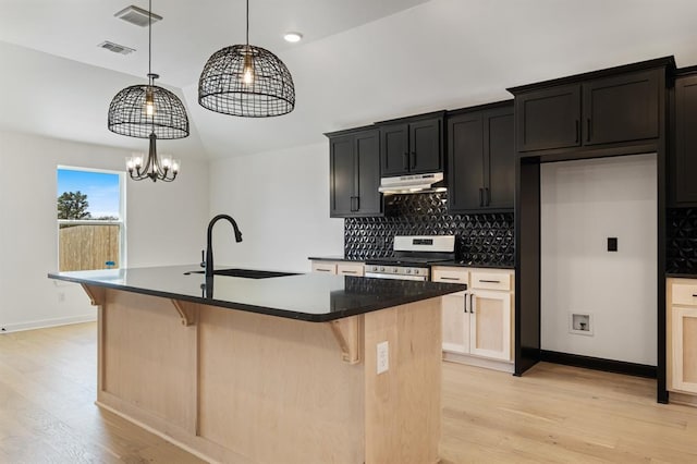 kitchen featuring vaulted ceiling, stainless steel range, a center island with sink, and sink