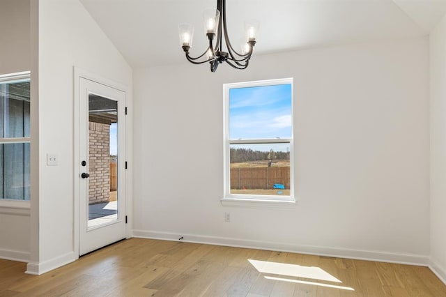 unfurnished dining area with a chandelier, vaulted ceiling, and light wood-type flooring