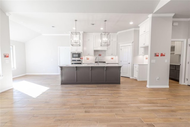 kitchen featuring built in microwave, sink, oven, pendant lighting, and a kitchen island with sink