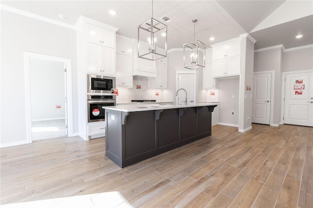 kitchen featuring stainless steel oven, white cabinetry, an island with sink, and built in microwave