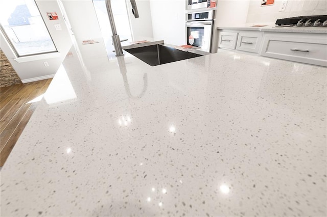 kitchen featuring light stone counters, stainless steel oven, gas stovetop, wood-type flooring, and white cabinets