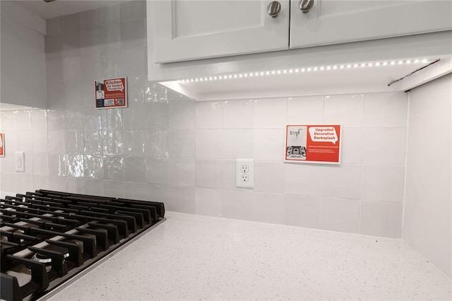 details featuring backsplash, light stone countertops, white cabinets, and gas cooktop