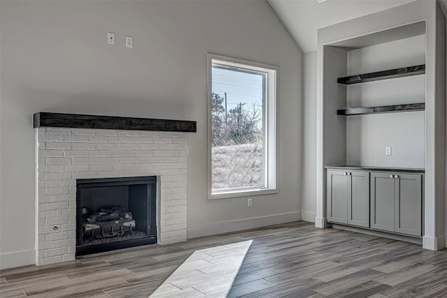 unfurnished living room with a wealth of natural light, light wood-type flooring, vaulted ceiling, and a brick fireplace