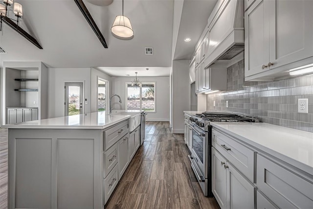 kitchen featuring dark wood-type flooring, premium range hood, an island with sink, pendant lighting, and high end stainless steel range