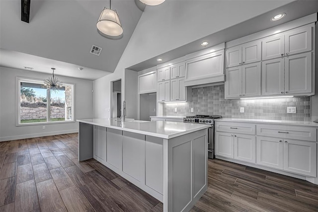 kitchen with dark hardwood / wood-style flooring, premium range hood, high end stainless steel range oven, decorative light fixtures, and a center island with sink