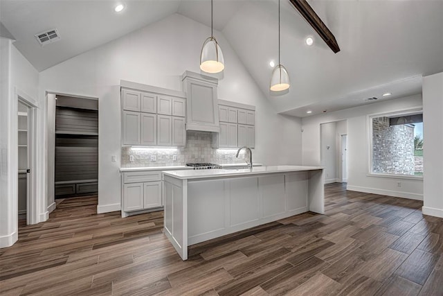 kitchen featuring backsplash, high vaulted ceiling, dark wood-type flooring, a center island with sink, and hanging light fixtures