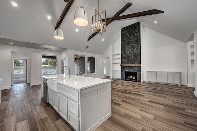 kitchen featuring pendant lighting, a kitchen island with sink, beamed ceiling, and dark wood-type flooring