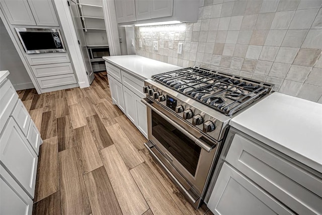 kitchen with tasteful backsplash, white cabinets, stainless steel appliances, and light wood-type flooring