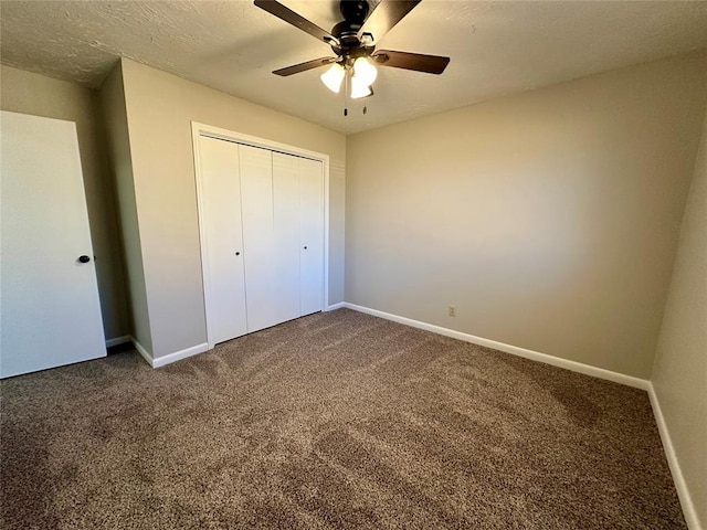 unfurnished bedroom with ceiling fan, a closet, a textured ceiling, and dark colored carpet