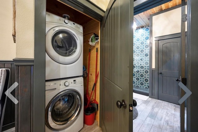 washroom with wood walls, light wood-type flooring, and stacked washer and dryer