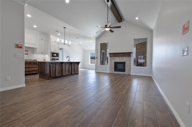 unfurnished living room featuring sink, a stone fireplace, dark hardwood / wood-style flooring, beamed ceiling, and ceiling fan with notable chandelier