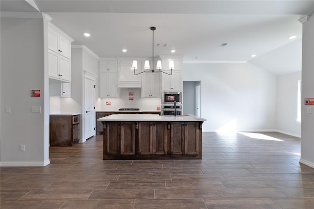 kitchen featuring pendant lighting, vaulted ceiling, an island with sink, appliances with stainless steel finishes, and a notable chandelier