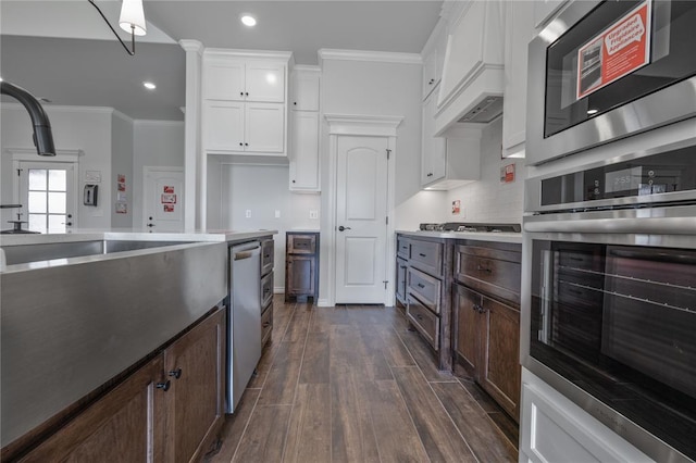 kitchen featuring appliances with stainless steel finishes, dark hardwood / wood-style flooring, dark brown cabinets, crown molding, and white cabinetry