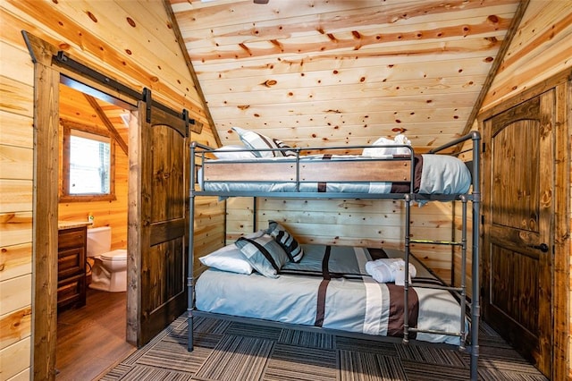 bedroom featuring lofted ceiling, ensuite bathroom, a barn door, and wood walls