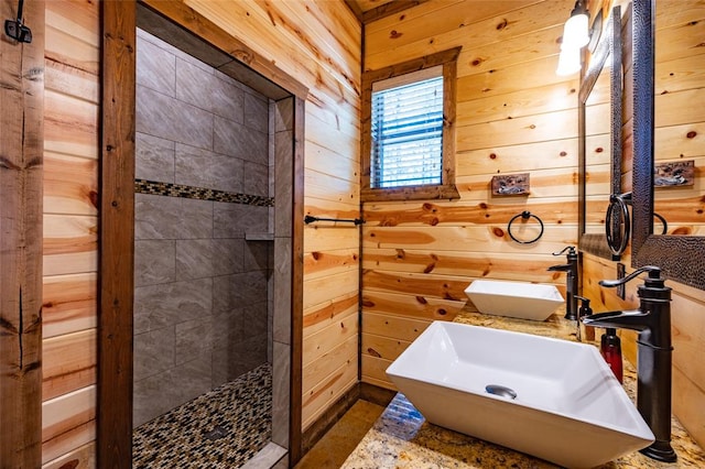 bathroom with a tile shower, sink, and wood walls