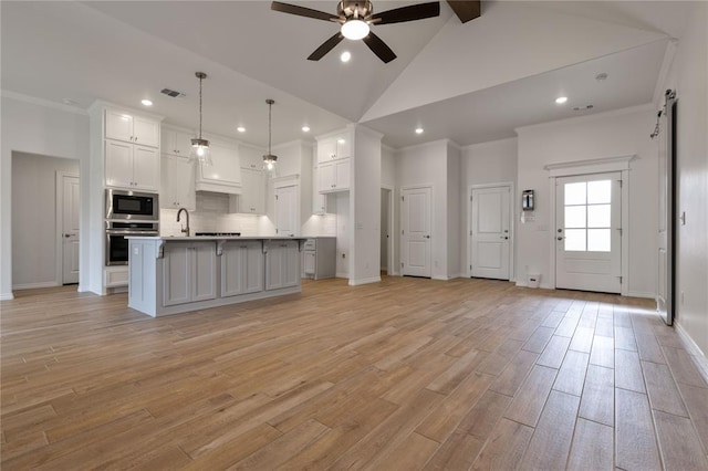 kitchen featuring a center island with sink, pendant lighting, white cabinetry, and appliances with stainless steel finishes