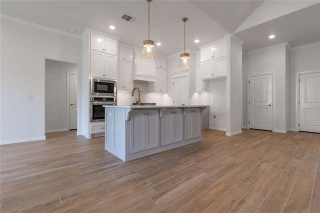 kitchen featuring appliances with stainless steel finishes, light wood-type flooring, a kitchen island with sink, pendant lighting, and white cabinetry