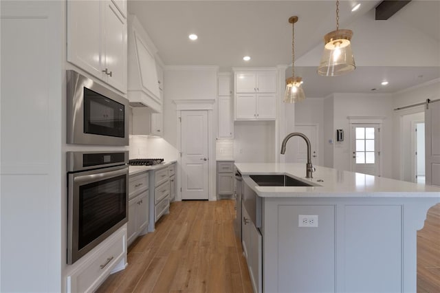 kitchen with pendant lighting, a center island with sink, sink, a barn door, and appliances with stainless steel finishes