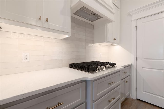 kitchen with decorative backsplash, dark hardwood / wood-style flooring, premium range hood, white cabinetry, and stainless steel gas stovetop