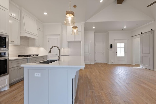 kitchen with pendant lighting, a kitchen island with sink, a barn door, light wood-type flooring, and stainless steel appliances