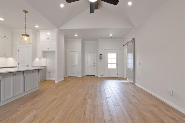 unfurnished living room with light hardwood / wood-style floors, ceiling fan, a barn door, and lofted ceiling