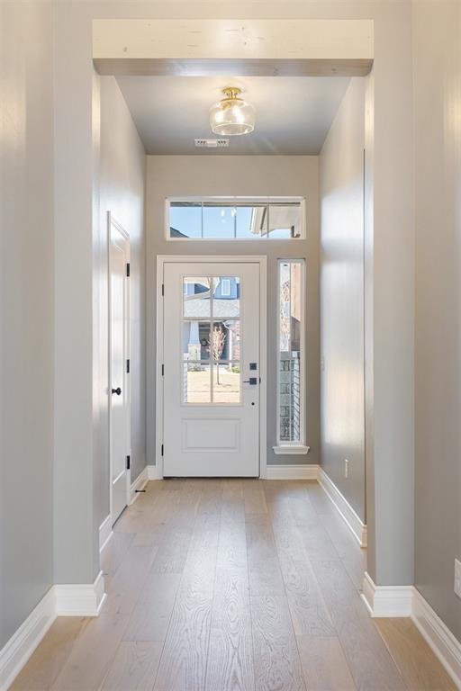 doorway to outside featuring beam ceiling and light hardwood / wood-style flooring