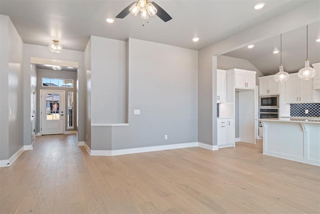 kitchen featuring pendant lighting, stainless steel microwave, backsplash, light hardwood / wood-style flooring, and white cabinetry