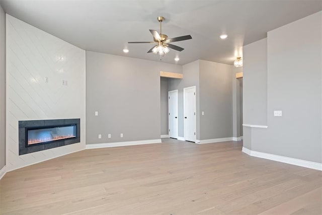 unfurnished living room with ceiling fan, a large fireplace, and light wood-type flooring