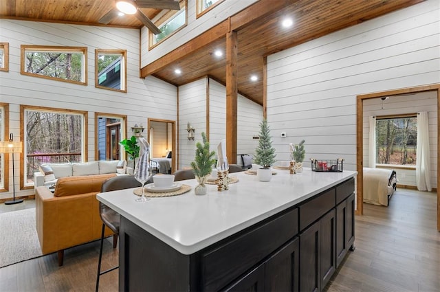 kitchen with wooden ceiling, high vaulted ceiling, hardwood / wood-style floors, wooden walls, and a kitchen island